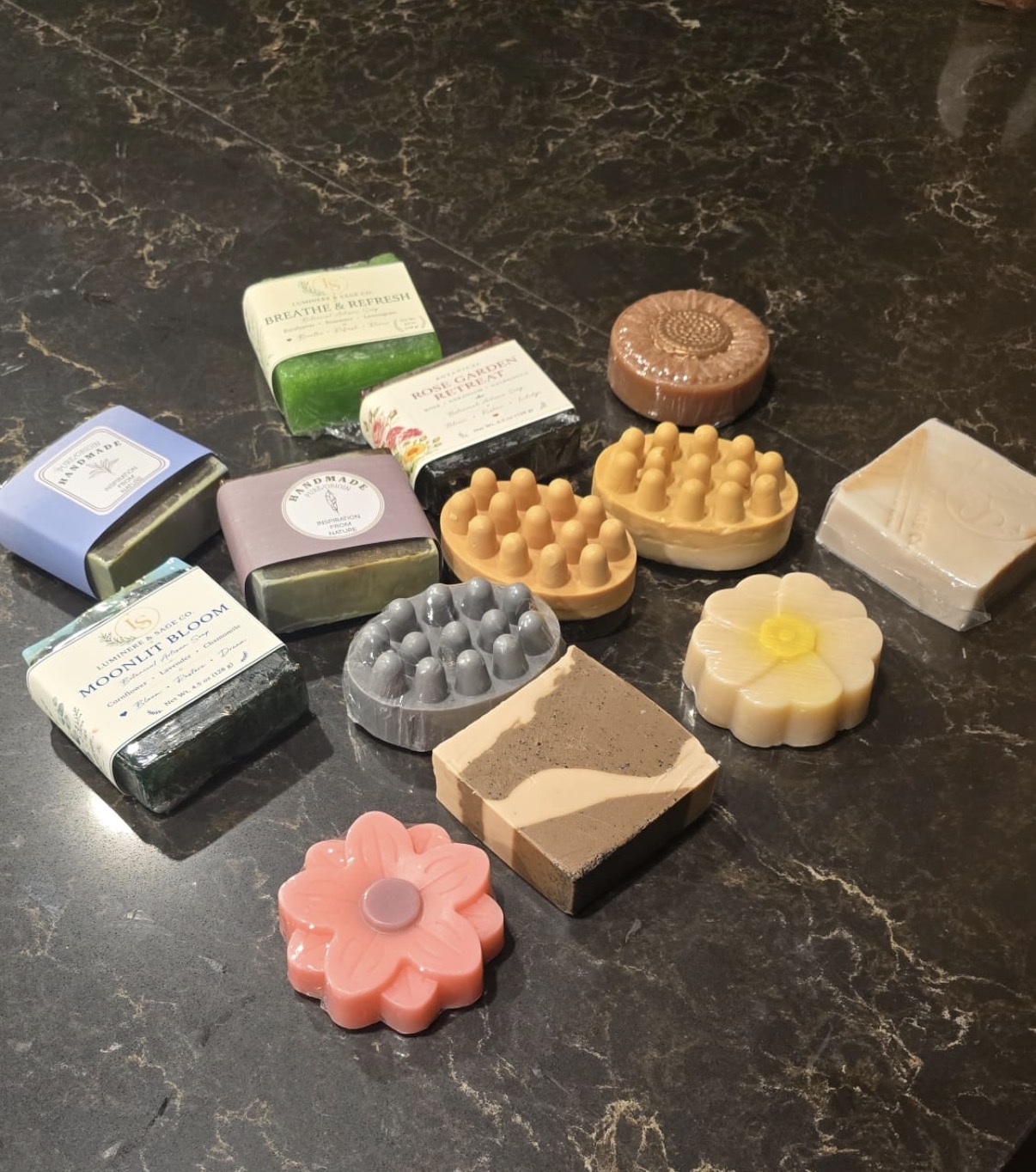 Wrapped rectangular bars, massage-shaped and daisy-shaped soaps on dark stone