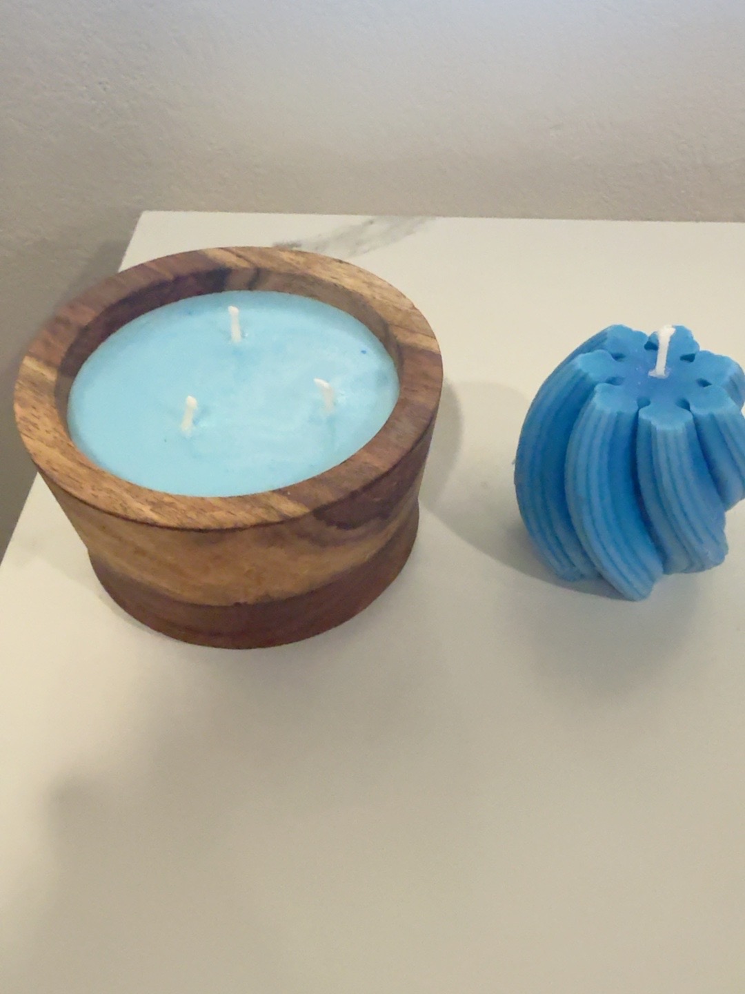 Blue three-wick candle in a wooden vessel beside a sculptural blue candle
