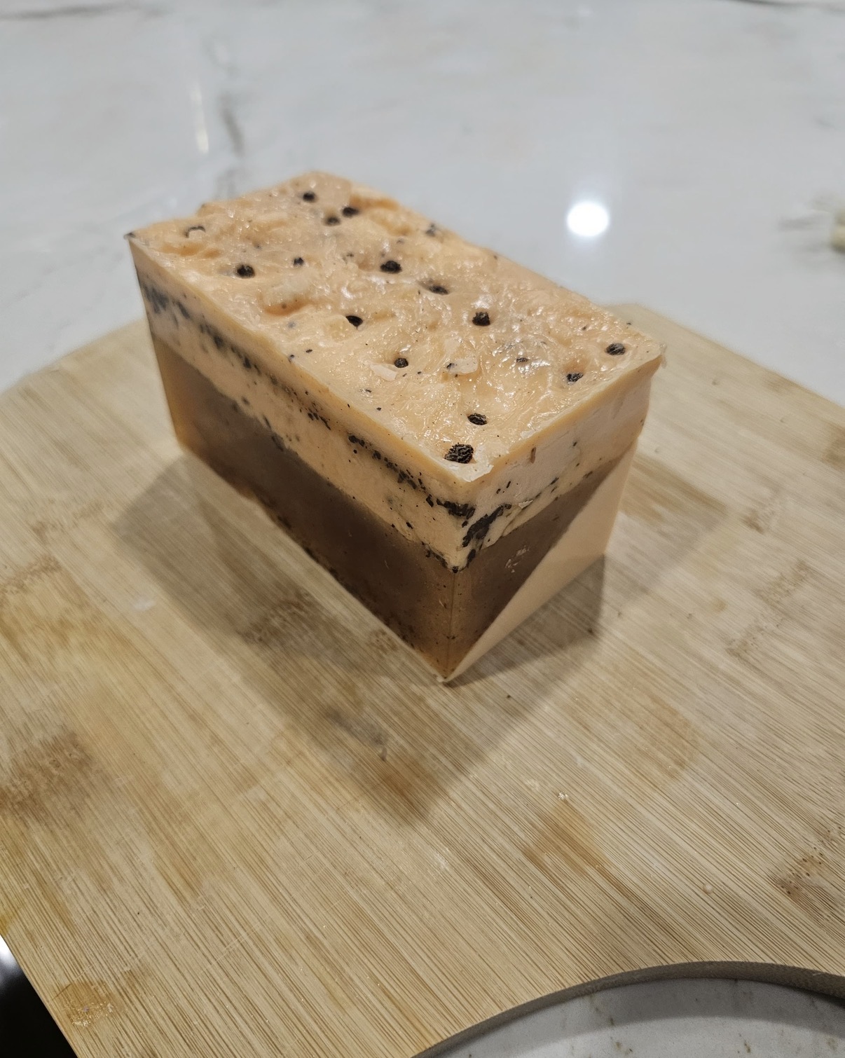 Cream and brown layered rectangular soap bar with dark flecks on a wooden board