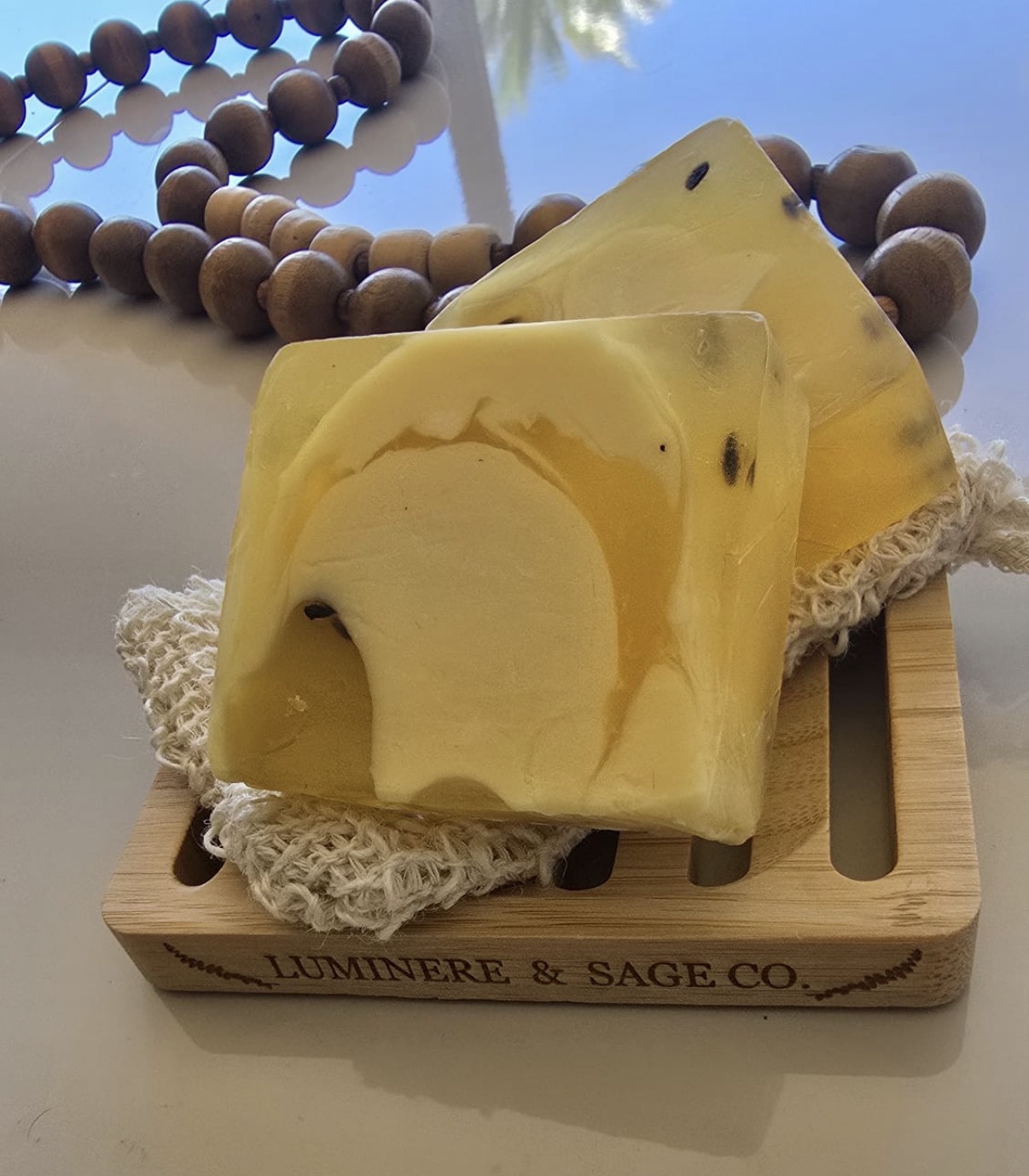 Two golden and yellow swirled square soap bars on a Luminere & Sage branded bamboo dish