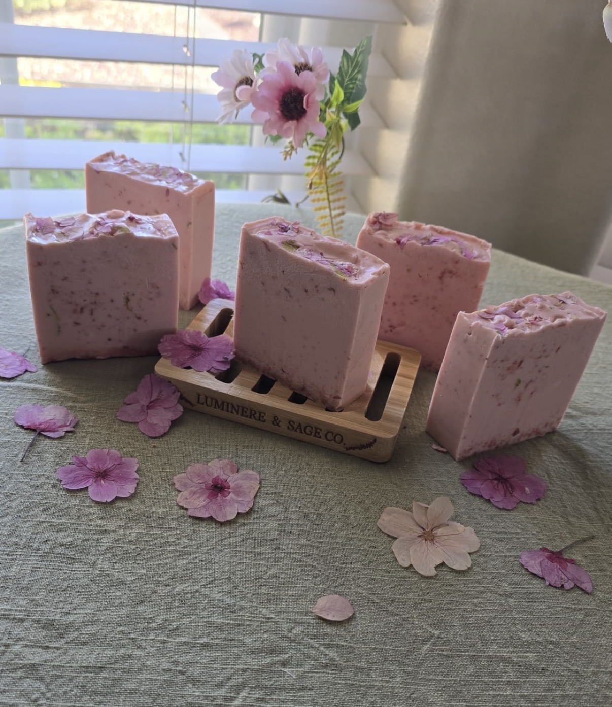 Pink soap bars with petal decorations arranged around a branded bamboo dish