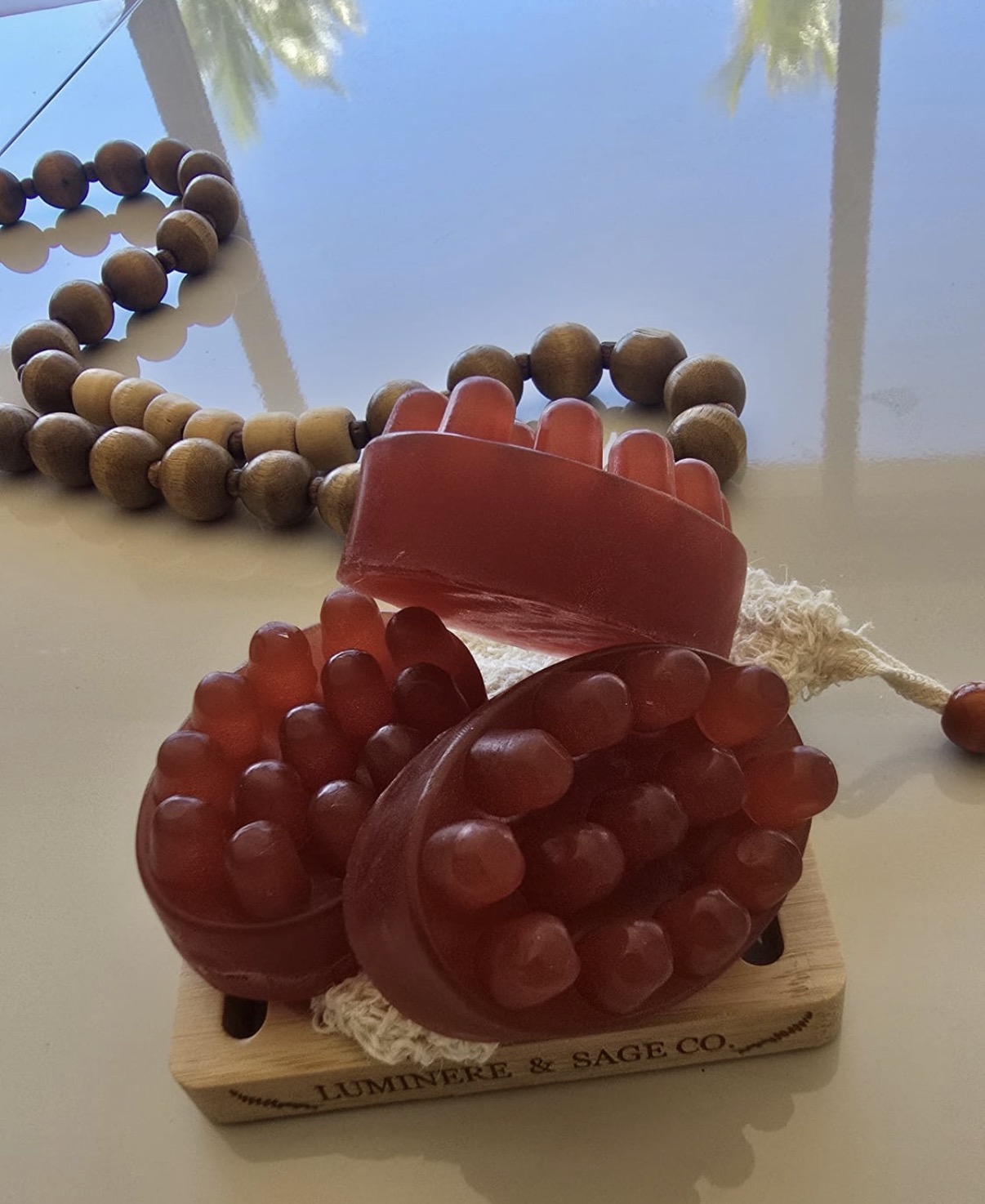 Red massage-shaped facial soaps arranged on a branded tray with wood bead decor