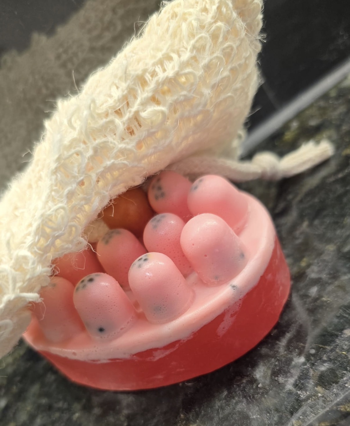 Pink and red layered massage-shaped facial soap partly inside a cream pouch