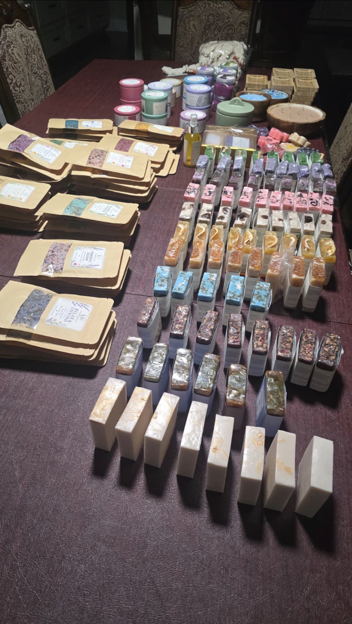 Long table arranged with kraft pouches, rows of wrapped soap bars, colored jars and tins