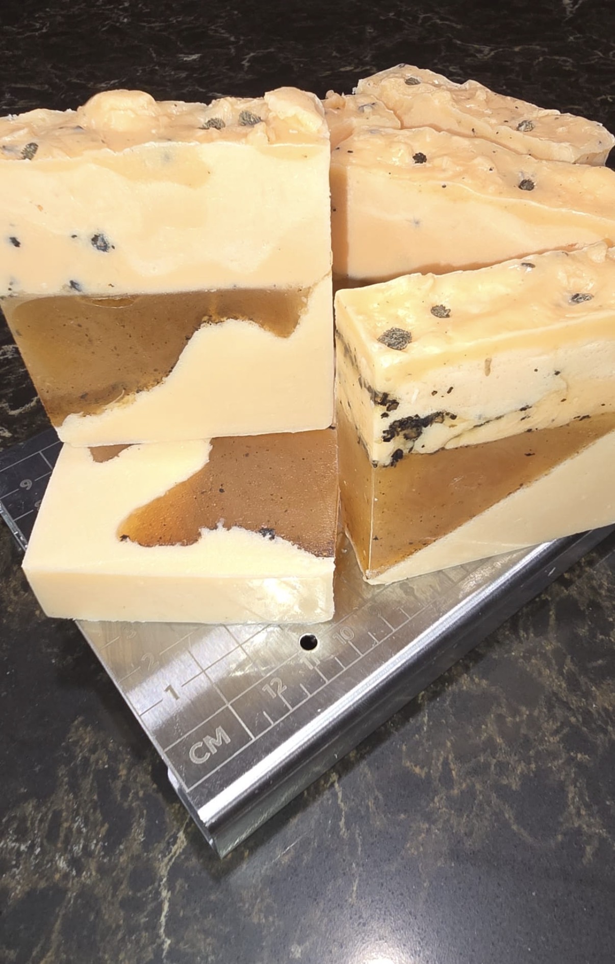 Cream and brown layered soap loaf and slices with dark flecks on a cutting guide